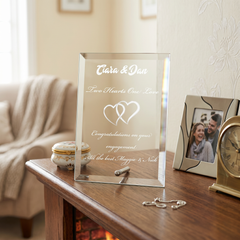 a clear glass frame with a personalized message, placed on a wooden table next to a picture frame and a clock.