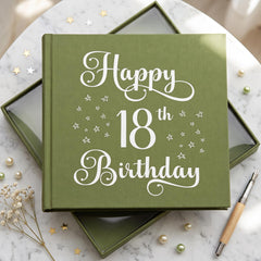 A green book titled "Happy 18th Birthday" with white stars on the cover, placed on a marble surface with scattered pearls and a pen.