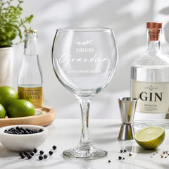 a personalized glass with the inscription "Fabulous Grandma" and "Love from Helen", surrounded by various alcoholic beverages and garnishes, such as a bottle of gin, a lime, and a bowl of blackberries.