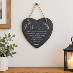 A black heart-shaped sign with a message hangs on a wall, accompanied by a potted plant and a lantern.