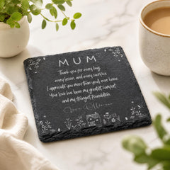 A slate coaster with a heartfelt message for a mother, accompanied by a cup of coffee and a potted plant, on a marble surface.