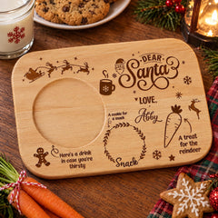 A wooden tray with a personalized message for Santa Claus, featuring a cookie, a carrot, and a snowflake design.
