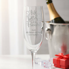 Friendship Champagne flute with engraved message next to a bottle of champagne and gift box on a white surface.