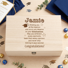 A wooden graduation gift box with a personalized message engraved on it, surrounded by graduation caps, confetti, and other graduation-related items.