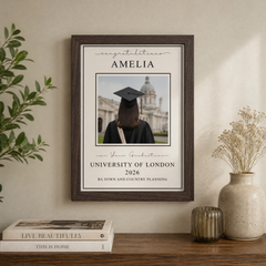 The image is a framed picture of a person wearing a graduation cap, with the text "Congratulations Amelia" and "University of London 2026 BA Town and Country Planning" printed on it. The picture is hanging on a wall, and there are some books and a vase on a table below it.